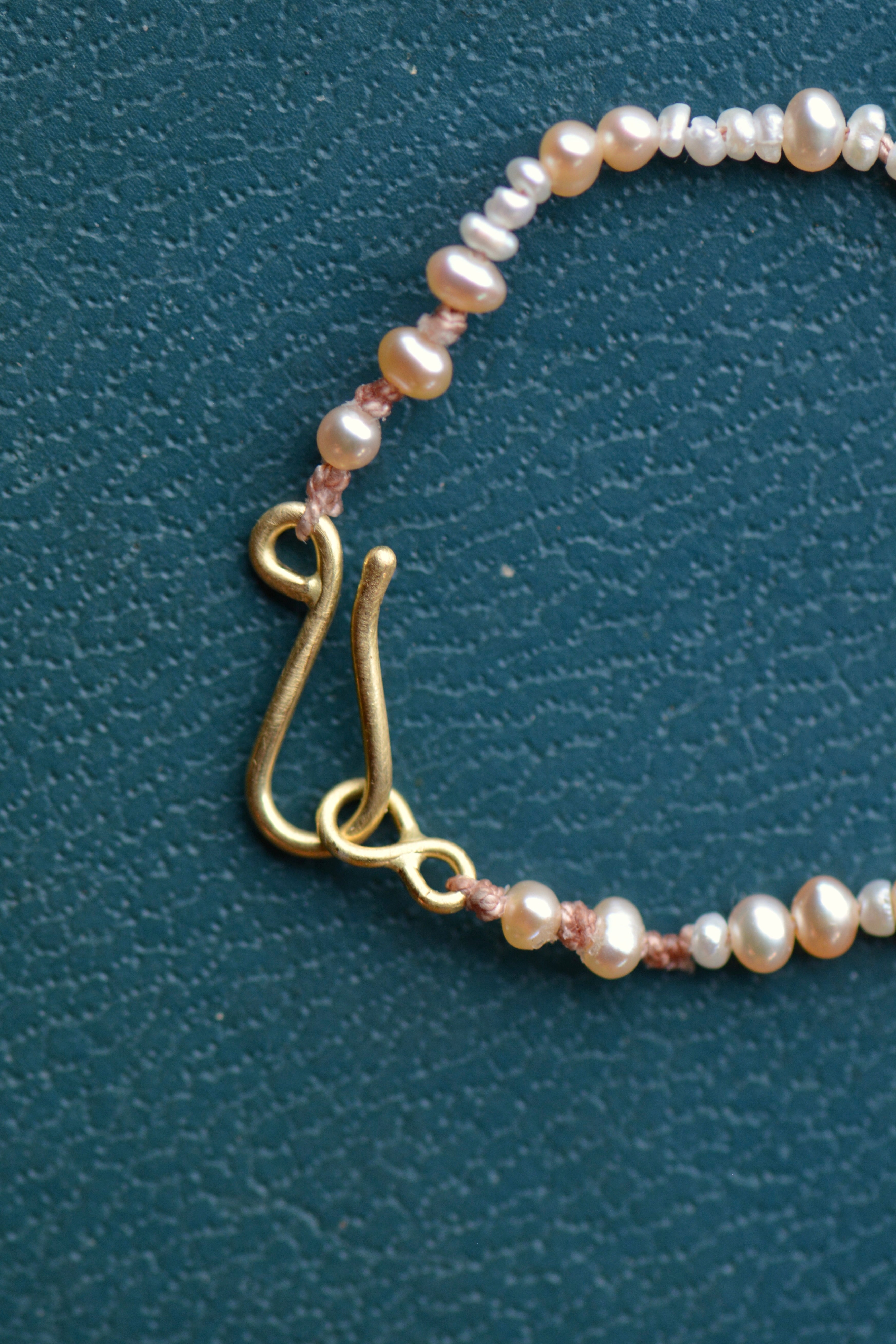 A close up image shows the handcrafted 18k gold clasp hook on a pearl beaded necklace.
