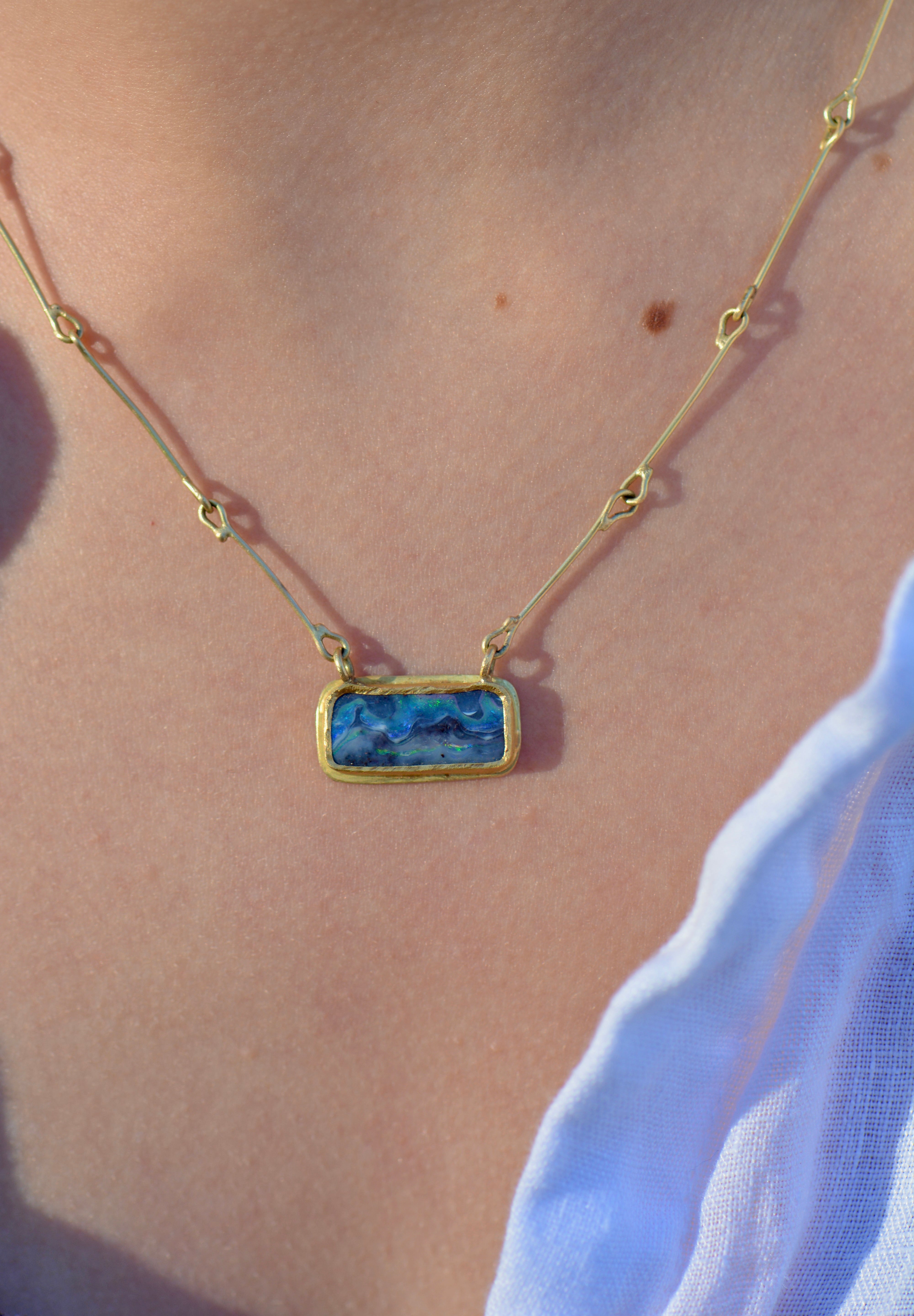 A close-up of a person wearing a delicate gold chain necklace with a rectangular blue stone pendant.