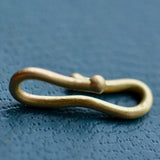 A gold charm connector hook sits on a teal blue textured backdrop.