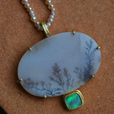 A sparkling dendritic agate oval stone with a blue and green flashing opal stone on the bottom, shown on a pearl beaded strand.