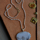 A dendritic agate and opal pendant is shown on a pearl beaded strand alongside a complimentary pair of mismatched dendritic agate and chrysoberyl earrings, all set in solid gold.