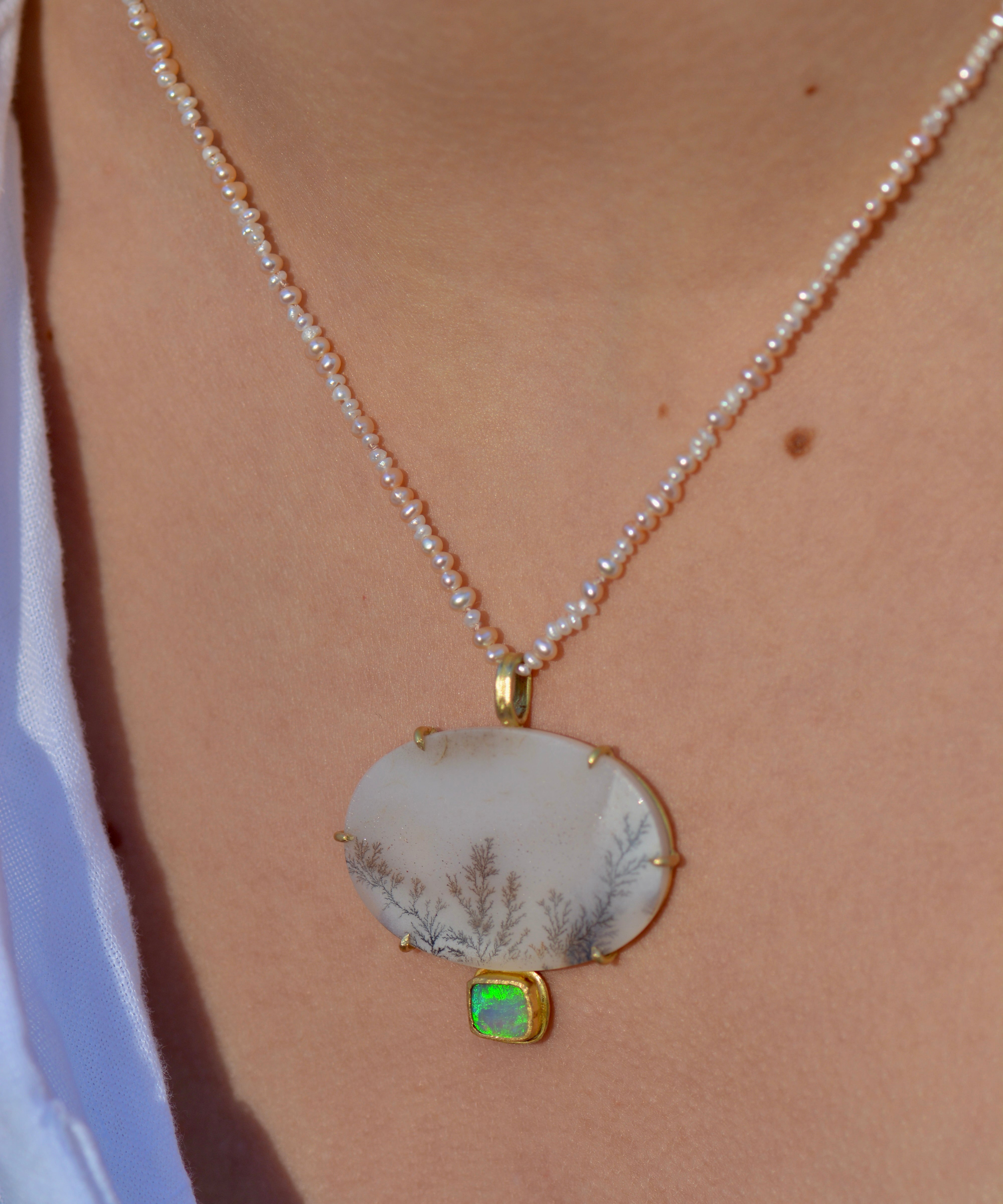 A unique dendritic agate and opal statement pendant is worn around the neck on a beaded pearl strand.