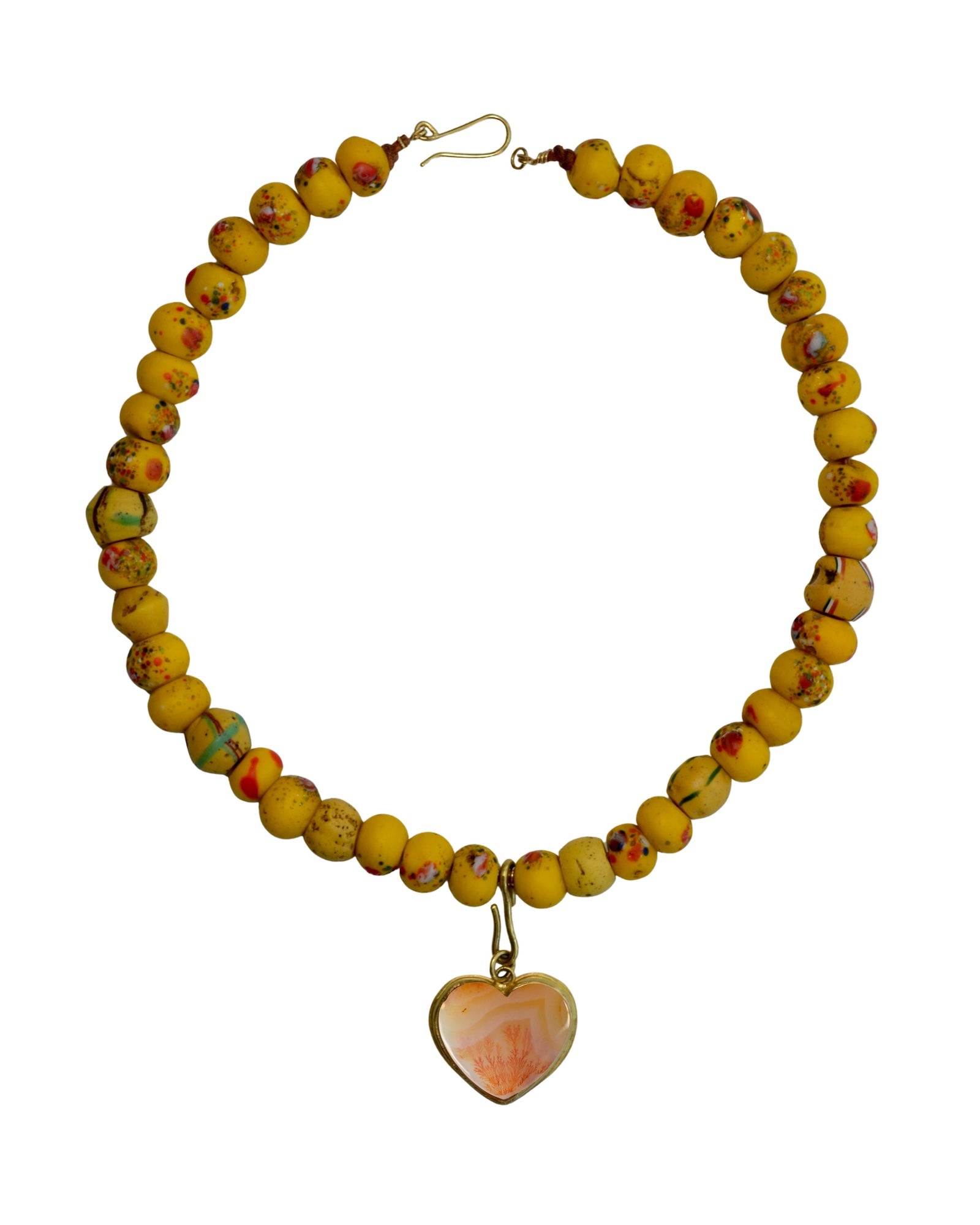 A beaded necklace made of round yellow beads with small red and green speckles, featuring a dangling heart-shaped pendant with a peach and white marbled pattern and a gold setting, shown on a plain white background.