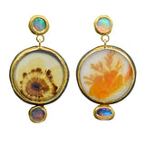A pair of gold dangle earrings featuring dendritic agate cabochons with natural inclusions, one with a brown radiating pattern and the other with orange coral-like structures, each accented with small round iridescent opal stones at the top and bottom.