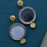 A pair of statement earrings in oxidized silver and solid gold are shown from the back, showing their post and butterfly closure and open settings behind the agates allowing light to glow through and keeping the earrings lightweight.