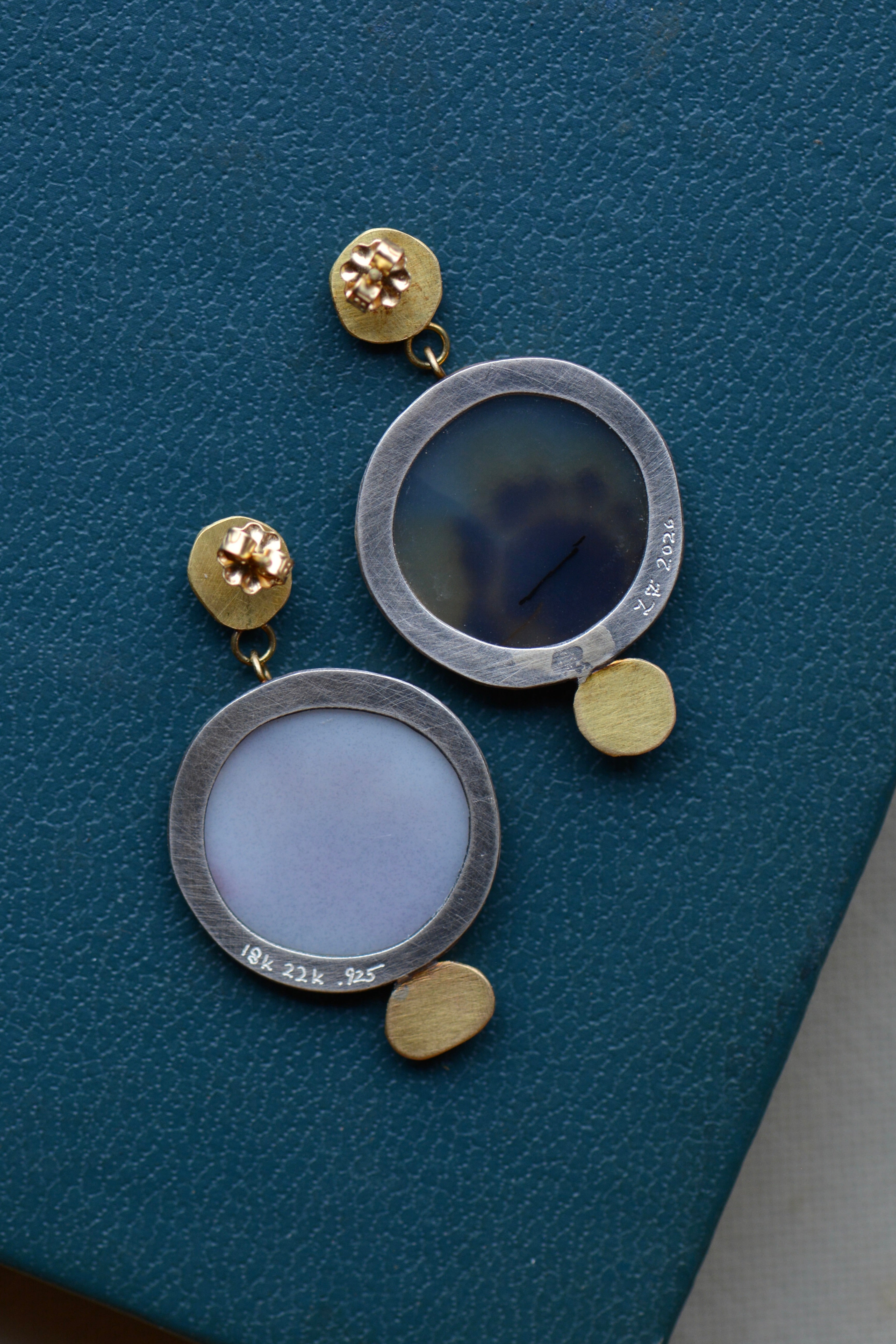 A pair of statement earrings in oxidized silver and solid gold are shown from the back, showing their post and butterfly closure and open settings behind the agates allowing light to glow through and keeping the earrings lightweight.