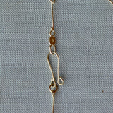 A close-up of a gold chain necklace laid flat on a textured light gray fabric background.