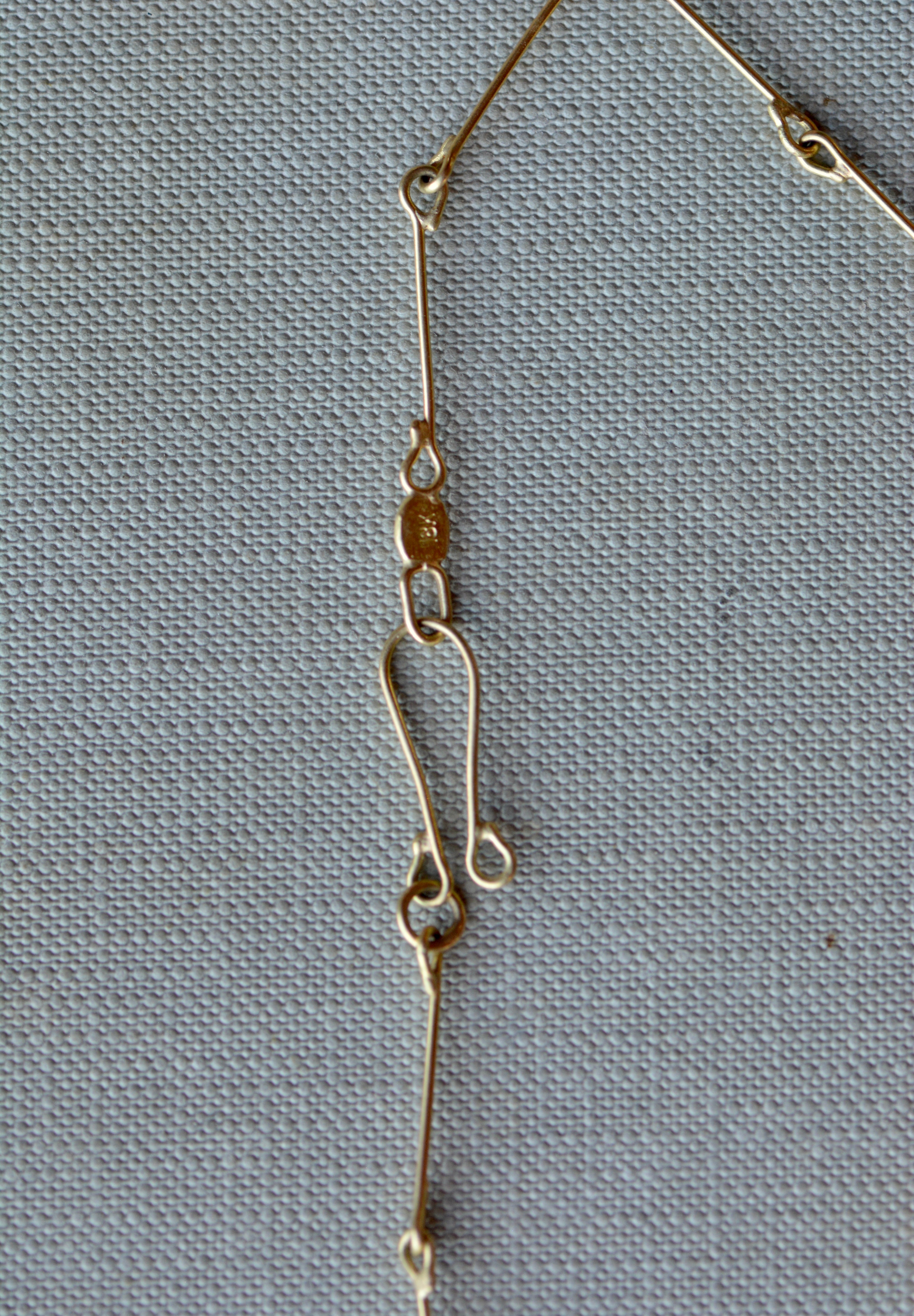 A close-up of a gold chain necklace laid flat on a textured light gray fabric background.