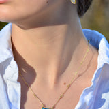 A close-up lifestyle shot of a woman wearing a gold handcrafted necklace with a blue rectangular stone pendant and a matching opal and gold drop earring.