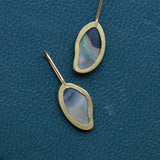 The reverse of a pair of opal earrings set in gold shows open backs and gold hook earwires.