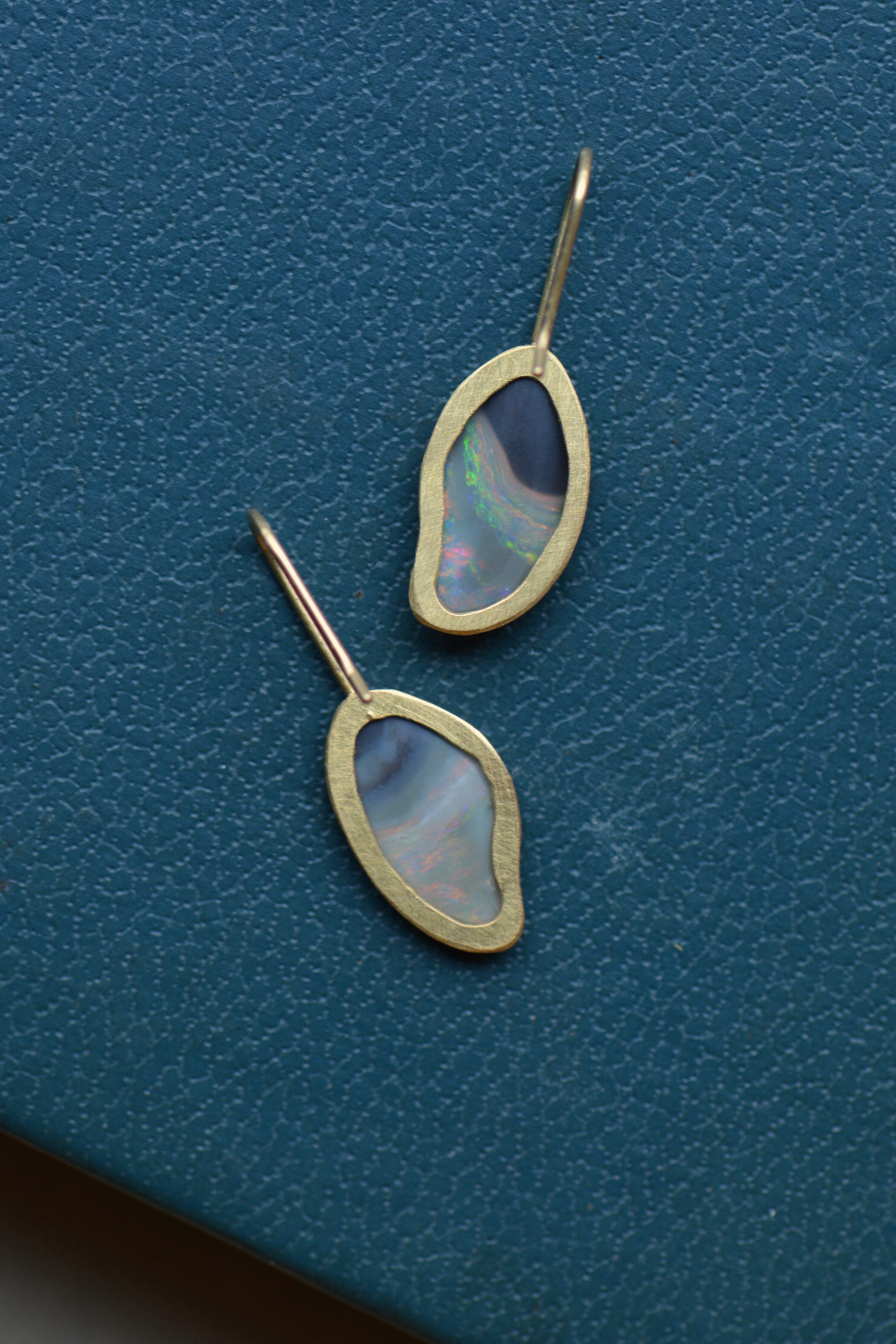 The reverse of a pair of opal earrings set in gold shows open backs and gold hook earwires.