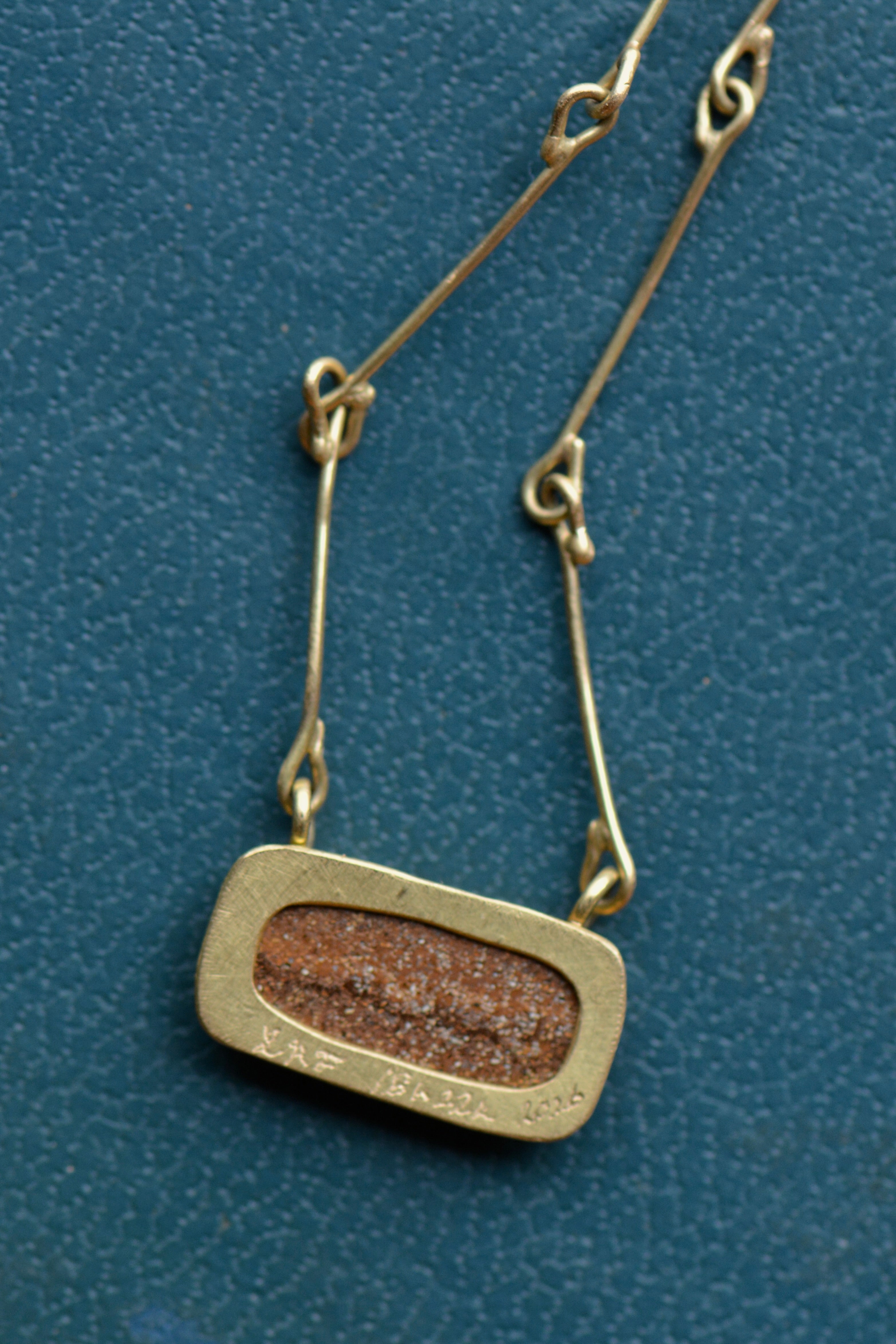 The reverse side of a necklace shows the gold setting cutout to reveal the brown textured back of the stone.