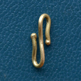 A gold charm connector hook sits on a teal blue textured backdrop.