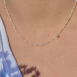 A delicate beaded seed pearl necklace worn by a model, shown in a close-up shot of the neck and chest area.