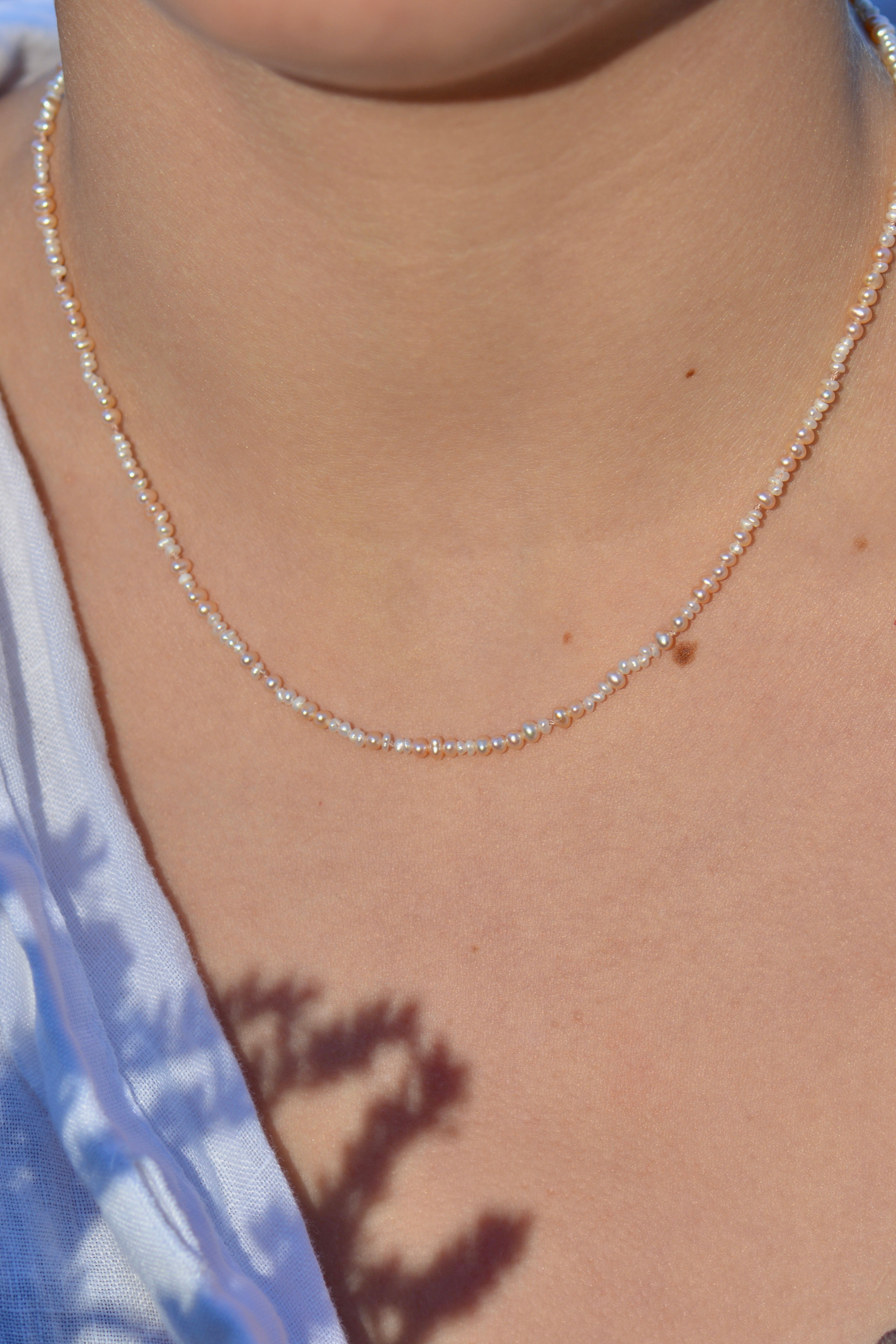 A delicate beaded seed pearl necklace worn by a model, shown in a close-up shot of the neck and chest area.