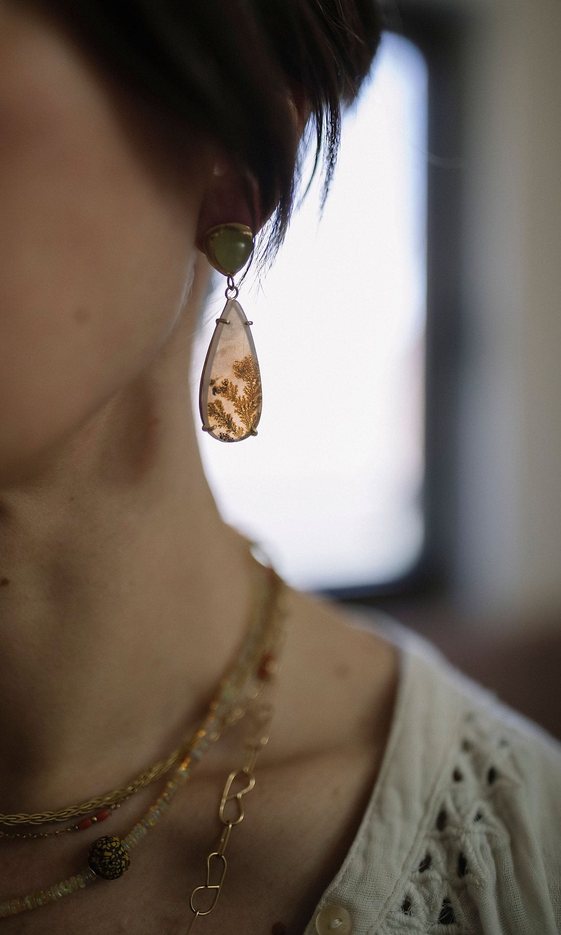 Dendritic agate and peridot drop earring with layered gold chains, worn