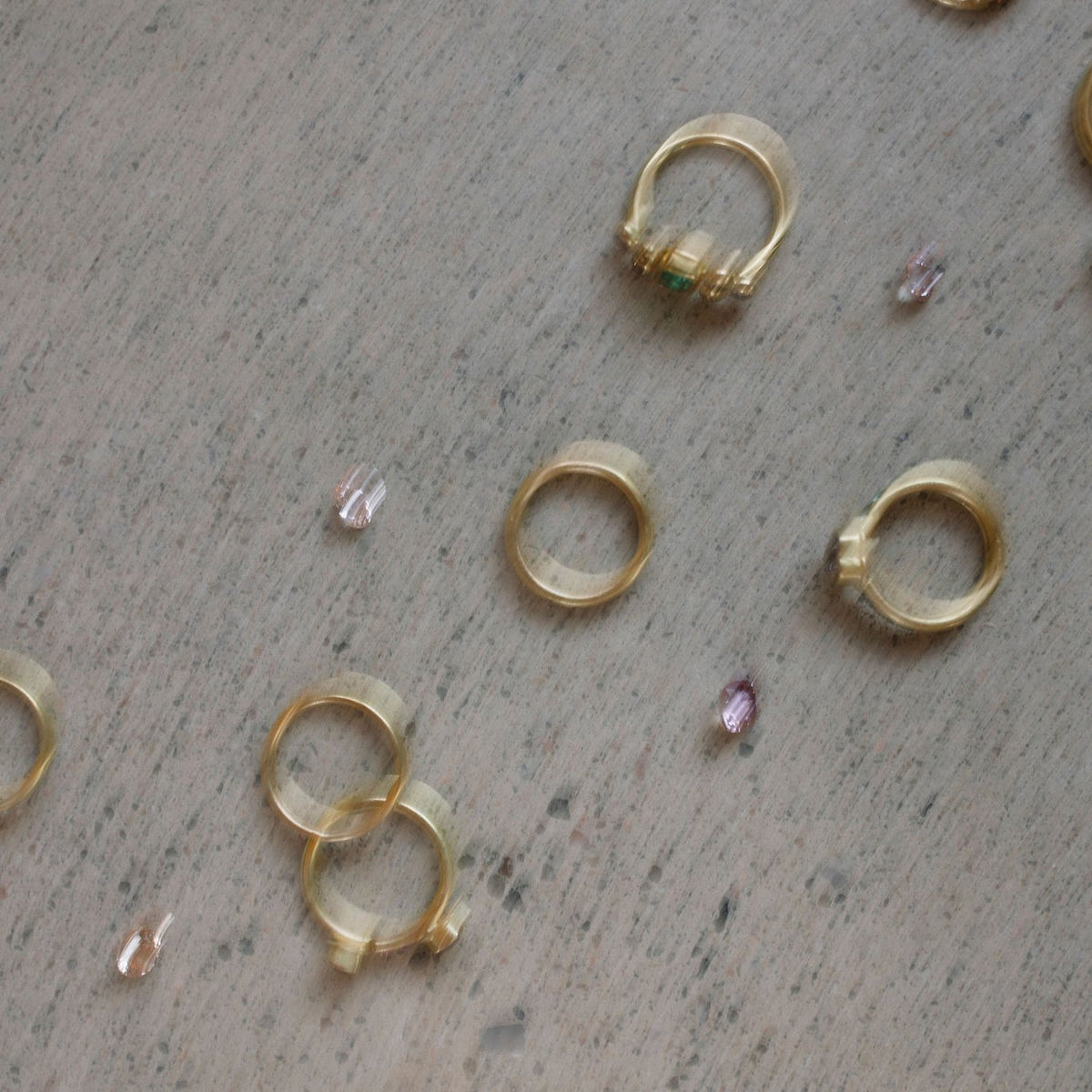 Gold rings and loose gems on a stone surface